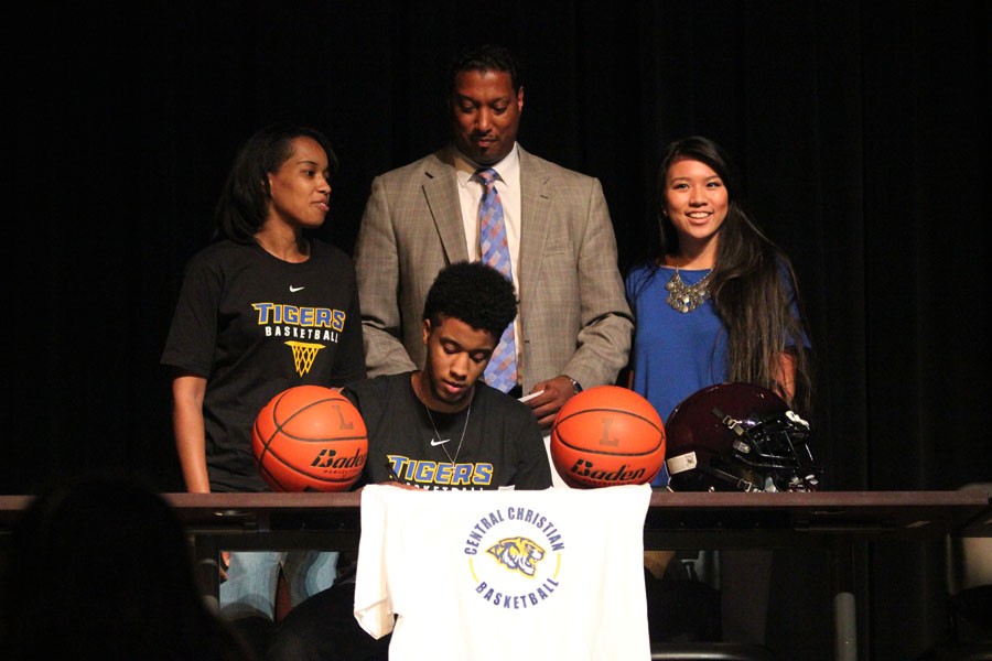 Sean Guillory sits and signs to Central Christian as his parents and girlfriend stand behind him.