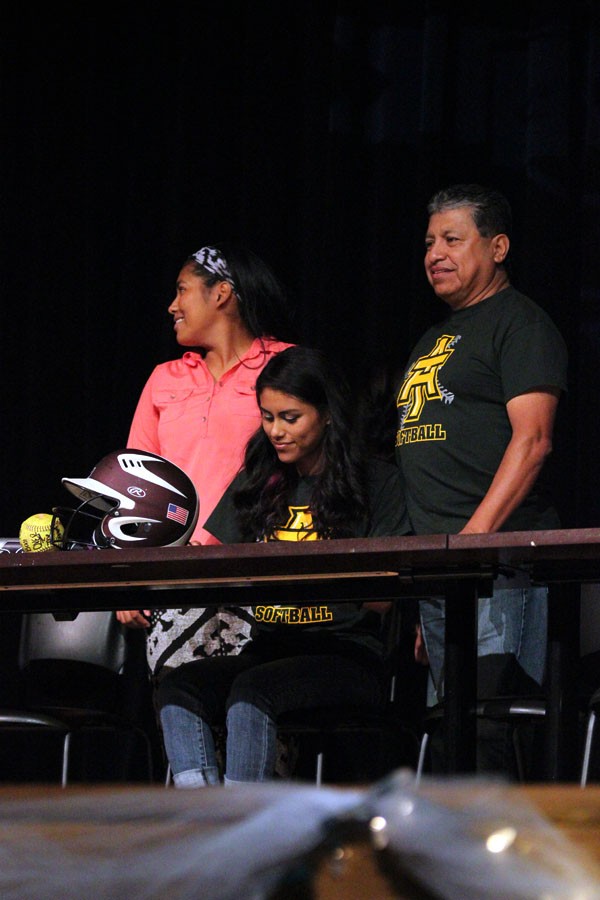 Softball catcher Gaby Vasquez signs to Arkansas Tech as family stand behind her smiling on. 