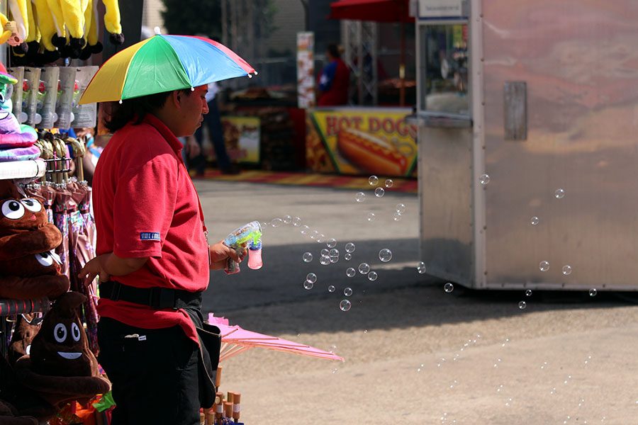 A fair worker blows bubbles in an attempt to attract fairgoers attention.