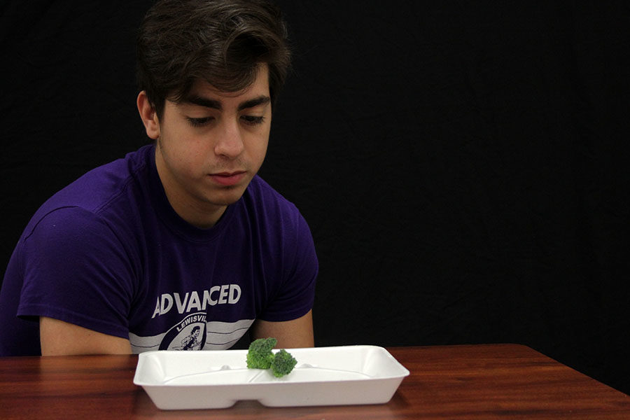 Junior Miguel Macias stares at a piece of broccoli to represent the eating habits of wrestlers.