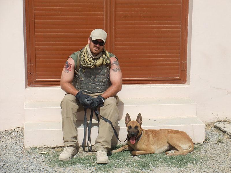 Former Navy sailor and law enforcement teacher Travis Mouser sits with a K-9 while in Afghanistan. Courtesy of Travis Mouser. 