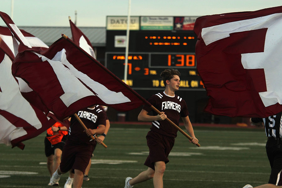 Senior cheer captain Caleb Tate runs and waves one of the Farmer flags.