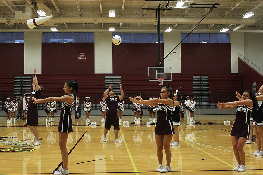 The cheerleaders perform their routine as they throw cones in the air.