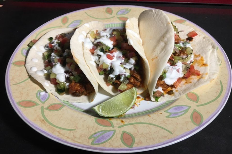 Three pork poblano tacos served with lime by senior Erick Nguyen sit on a plate.