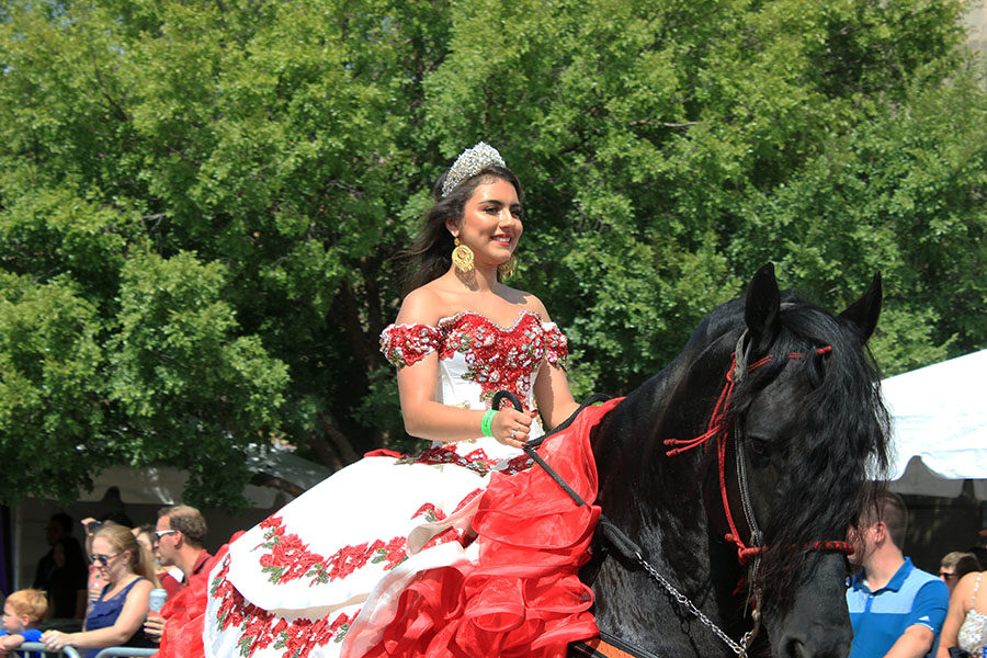 A girl dressed up in a quinceñera dress rides a horse during the parade.
