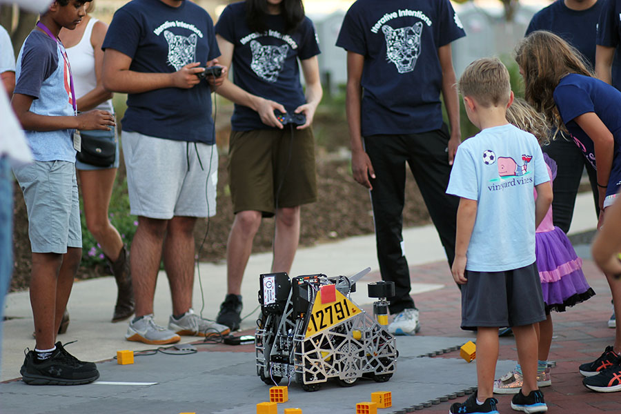 A group of teenagers show off a robot to younger kids.