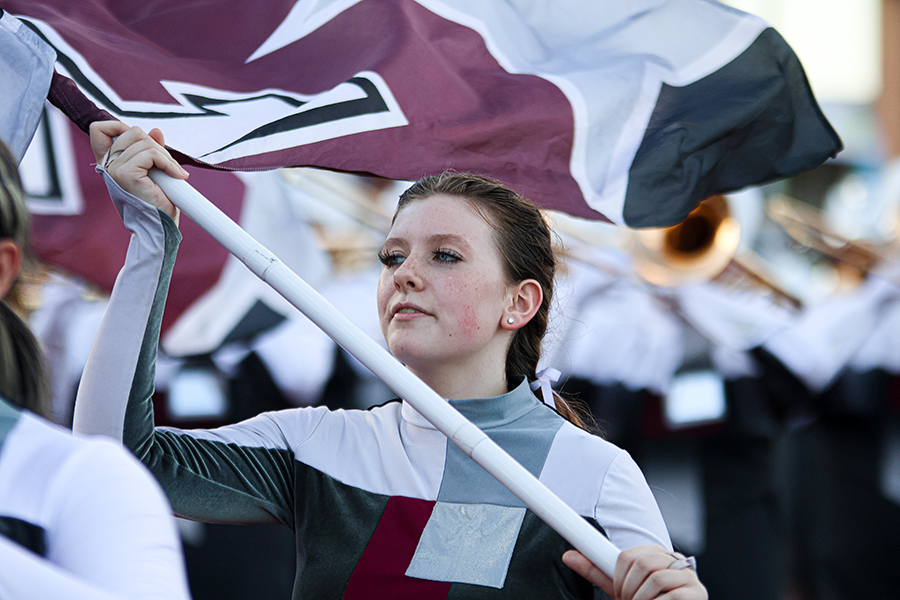 Sophomore Lillie Sherman swings her flag as she marches down the track before the football game on Sept. 22.