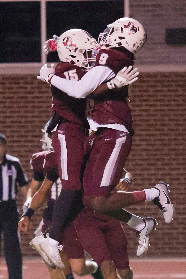 Running back Addison Wells (15) and wide receiver Lamar Kerby (9) share a hug while jumping in the air after Kerby ran the ball into the end zone to score a touchdown during the fourth quarter.